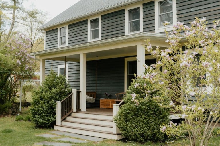 An older home with green-grey siding and off-white accents is a great example of a fixer-upper that has increased in value