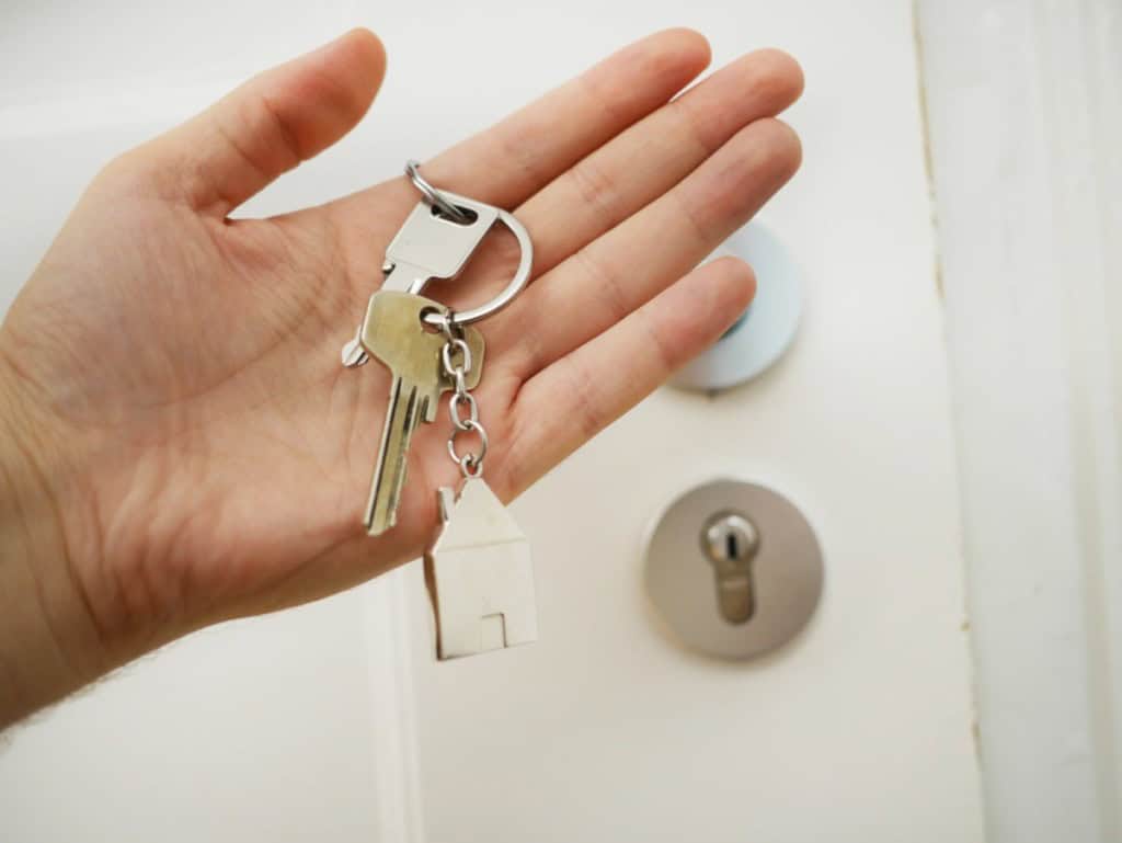 hand holding house keys to their own house in front of a door