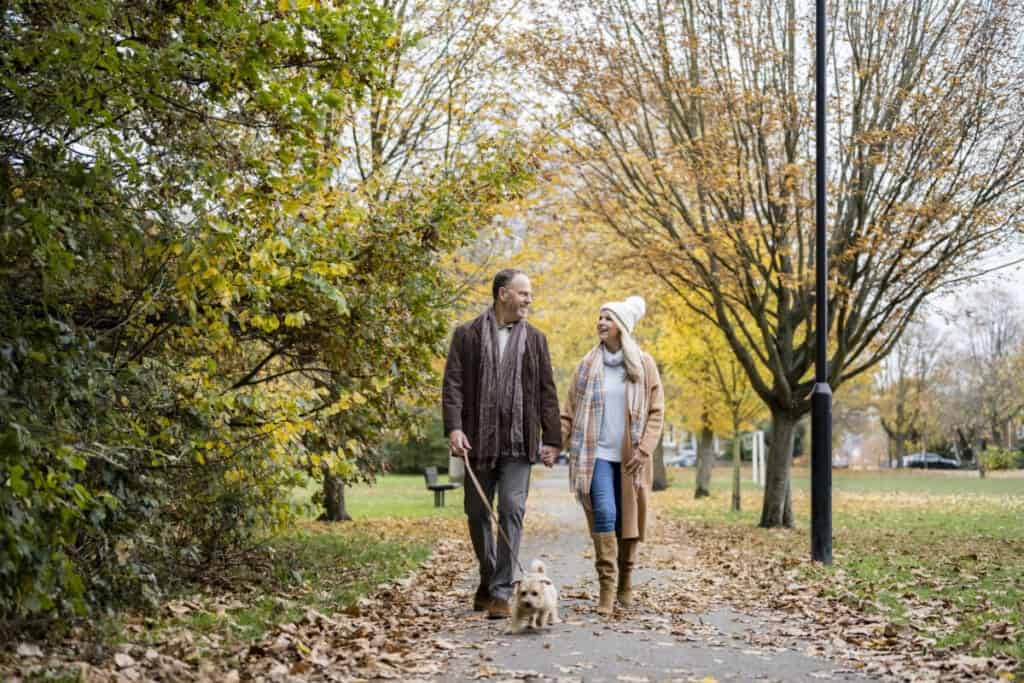 couple walking terrier on footpath in public park