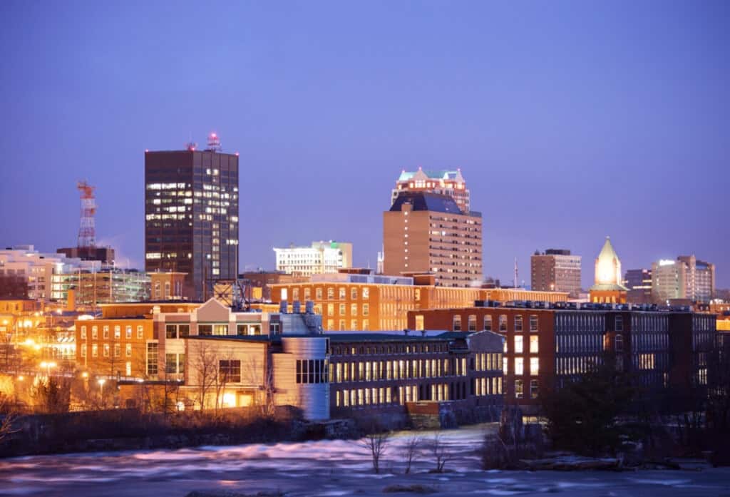 Manchester, New Hampshire skyline along the banks of the Merrimack River at night. Manchester is the largest city in the state of New Hampshire and the largest city in northern New England. Manchester is known for its industrial heritage, riverside mills, affordability, and arts & cultural destination.