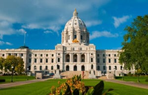 "Front view of the Minnesota State Capitol Building (the center of the State Government of Minnesota) in St. Paul, with a lawn, plants, and flowers in the foreground. The Minnesota State Capitol building was designed by Cass Gilbert with Italian Renaissance and Beaux Arts influences."