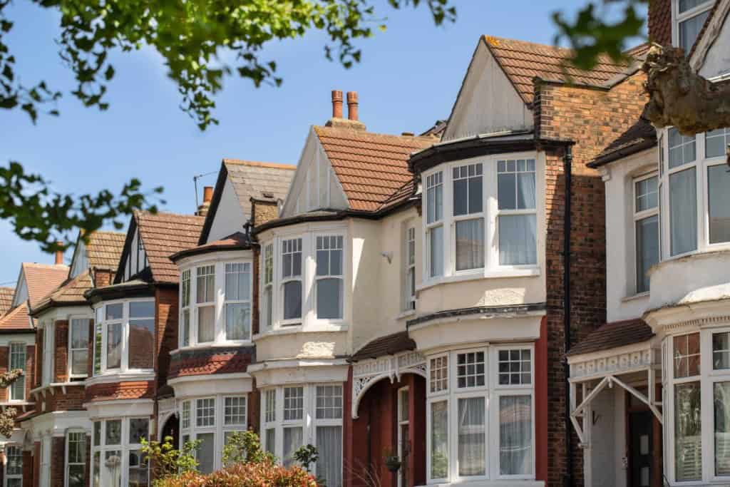 Lovely English Edwardian residential houses in a row with spectacular big wooden bay casement windows. Front view on the properties from the street with green trees on sunny day. London, UK