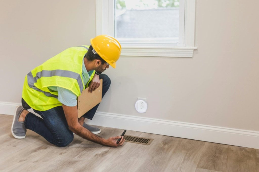 A man with a clipboard inspects a wall, likely during a home inspection or appraisal