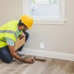 A man with a clipboard inspects a wall, likely during a home inspection or appraisal