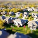 Aerial view of a planned suburban residential neighborhood with numerous modern houses and green lawns, representing communities that may be governed by both CDD and HOA regulations, with a tilt-shift effect making the scene appear miniature.