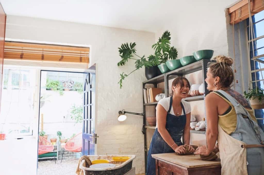 Two friends hand-building with clay together in a small but bright home pottery studio