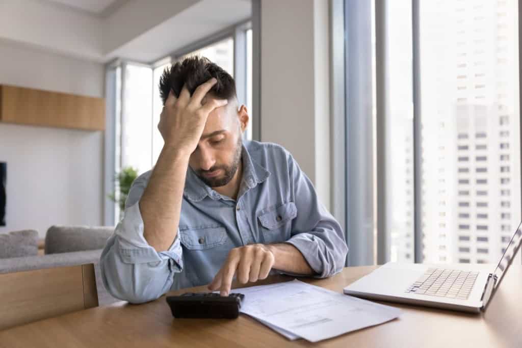 Worried tired homeowner getting financial problems, using calculator at home office workplace to calculate mortgage, touching head in frustration, finding bankruptcy risk, making difficult decision