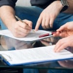 Close up of people's hands signing closing documents on a coffee table.