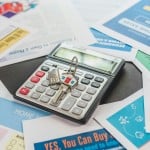 Calculator, keys and home buying literature laid out on a surface.