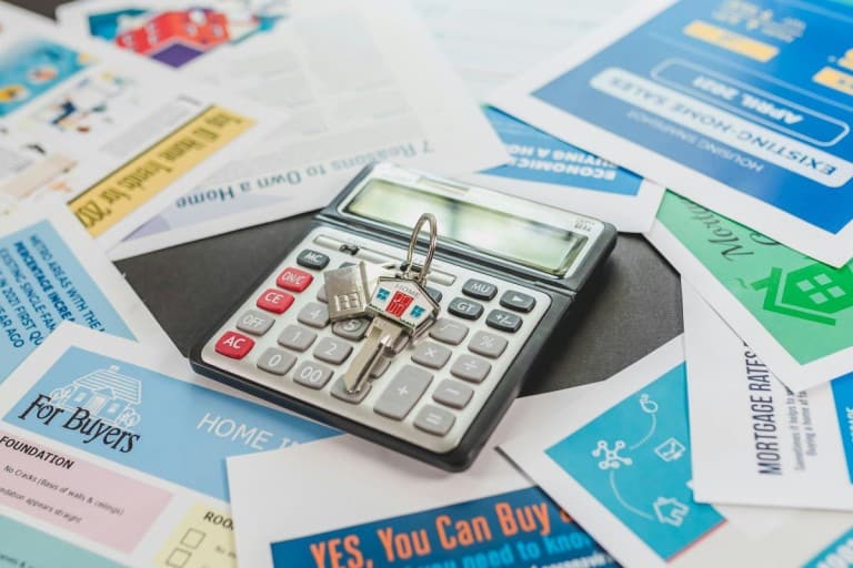 Calculator, keys and home buying literature laid out on a surface.