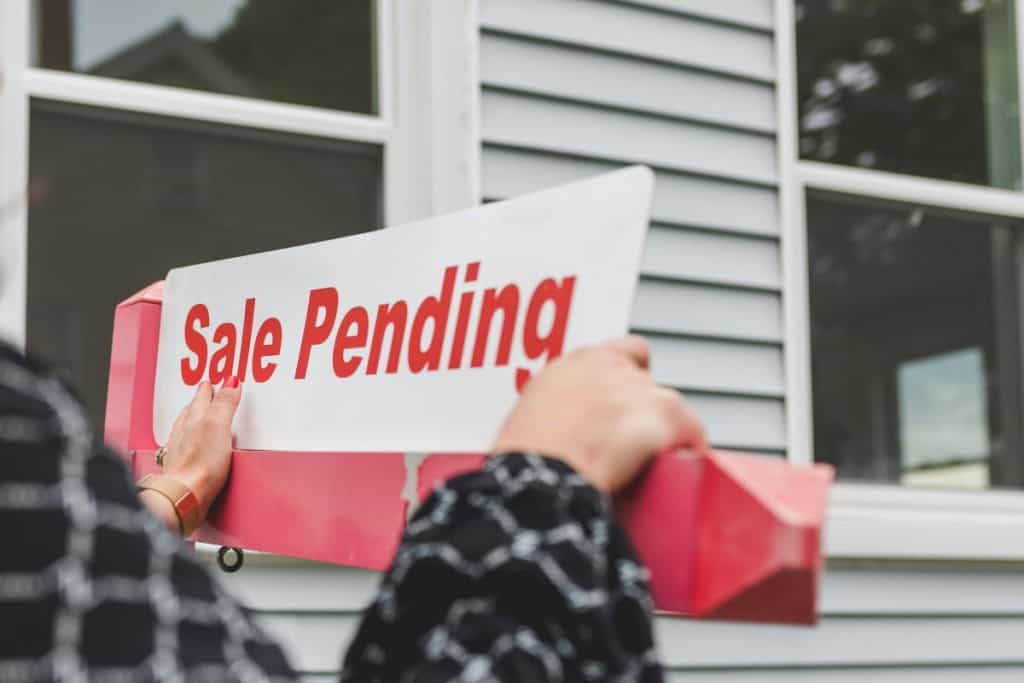Image of person adjusting a "sale pending" sign outside of a home, which may happen when a home is listed as active offer no bump.