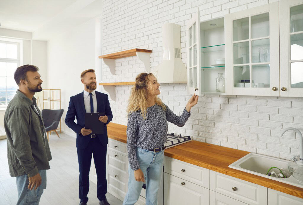 Realtor showing a young family around a kitchen, offering house hunting tips on checking appliances and finishes.