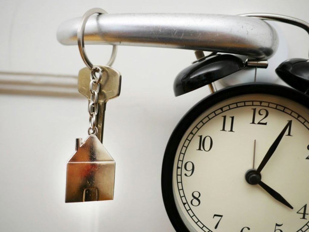 House keys hanging on door knob with a clock, illustrating good signs your house will sell if you know when to list it.