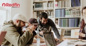 Use Redfin to learn how to rent an apartment as an international student. A group of students are gathered around a laptop in a study hall. They are laughing together.
