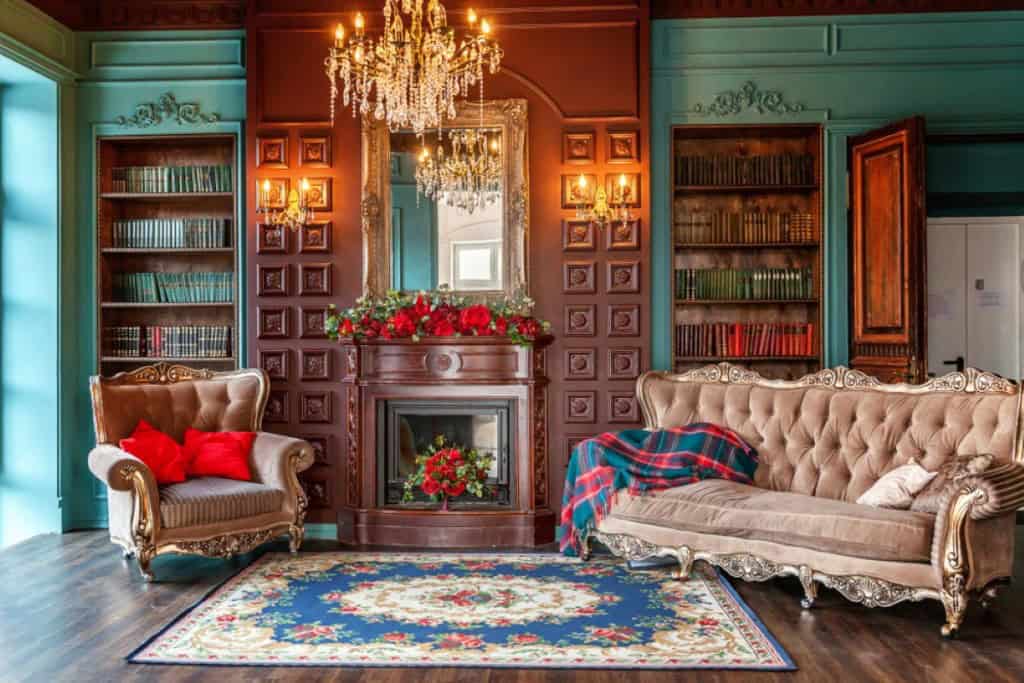 A vintage, Victorian-era living room color-bathed in a rich teal paint. Ornate bookshelves line the walls and cushy vintage seating completes the look.