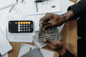 A person counting U.S. dollar bills beside a calculator and financial paperwork, representing how much earnest money is typically required in Texas real estate transactions.