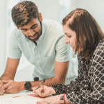Two people reviewing real estate photos at a table, discussing details related to Earnest Money vs. Option Fee during a home-buying process.