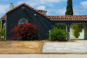 A Los Angeles stucco home painted a rich cobalt blue with a red tiled roof and big bushes out front.