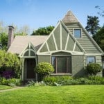 A bungalow style home, painted a soft green with white accents and a lush green lawn