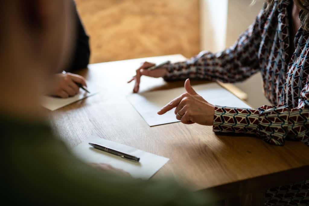 Three people sit around a table with partition action documents on it. One person is a partition lawyer who is explaining the documents to the other two people.