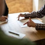 Three people sit around a table with partition action documents on it. One person is a partition lawyer who is explaining the documents to the other two people.