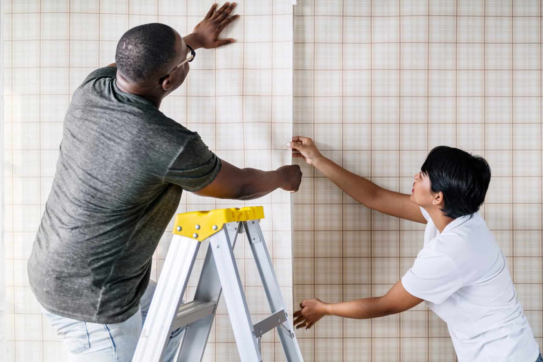 Two people are working on putting up wallpaper.