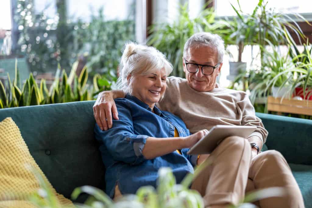 An older man and woman sit together on a couch looking at common reasons why people move to retirement communities.