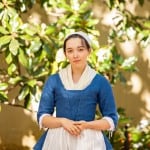 Costumed interpreter portraying Betsy Ross in an 18th-century blue dress and white cap