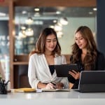 Two young women review documents and paperwork related to an investment property. Learn what to know before buying an investment property.