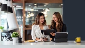 Two young women review documents and paperwork related to an investment property. Learn what to know before buying an investment property.