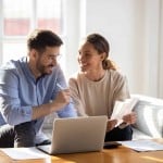 Couple reviewing financial paperwork and mortgage documents on a laptop while discussing what happens to your mortgage when you sell your house