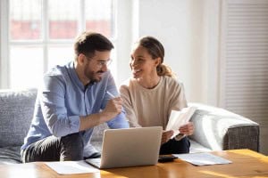Couple reviewing financial paperwork and mortgage documents on a laptop while discussing what happens to your mortgage when you sell your house